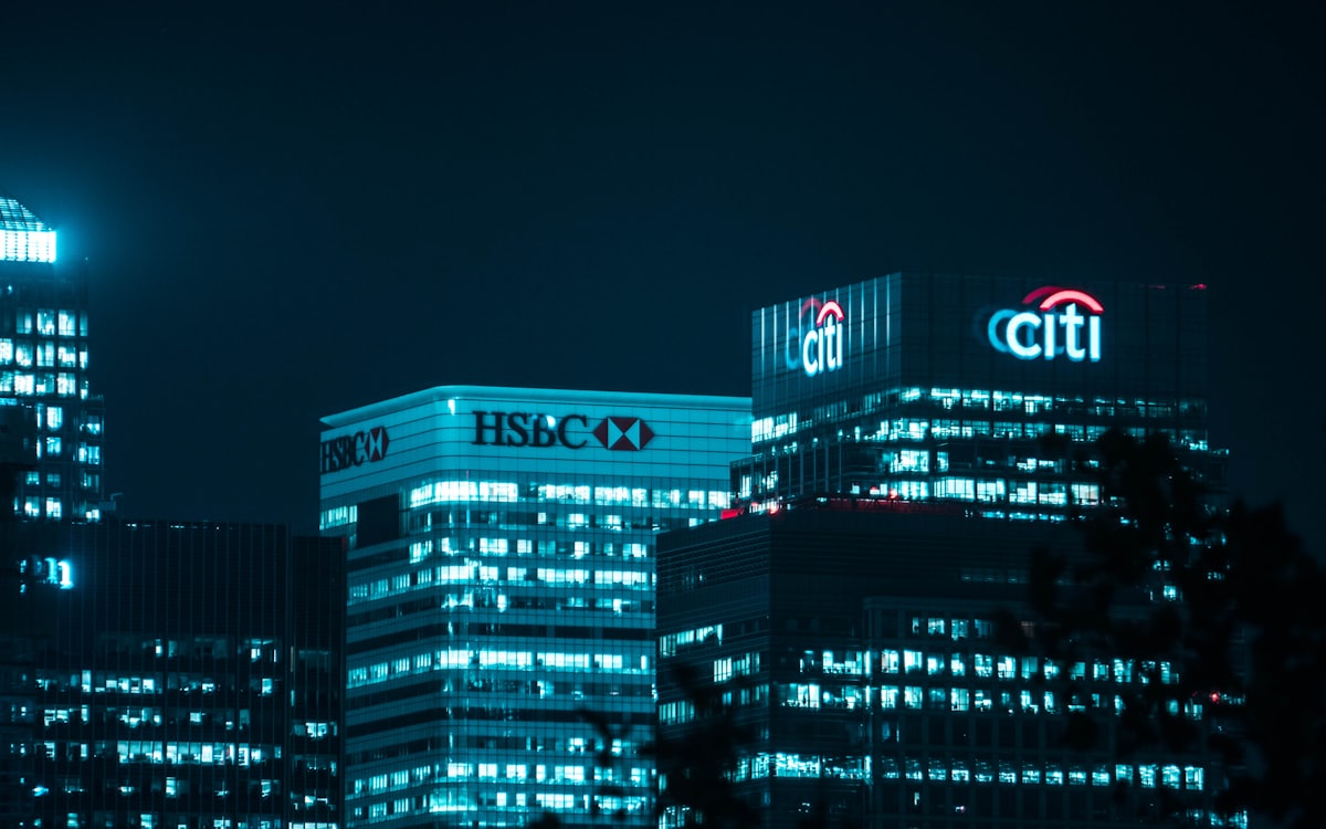 Black and white photograph of a financial district at night with bank signage on the towers
